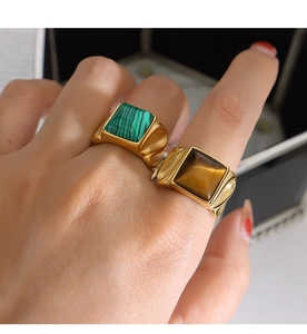 Detail von Tigerauge und Malachit auf goldenen Ringen, an Fingern getragen