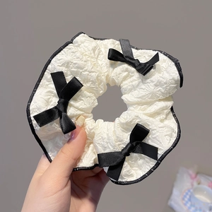 Détail d'un chouchou blanc gaufré avec bordure en dentelle noire et nœuds satin