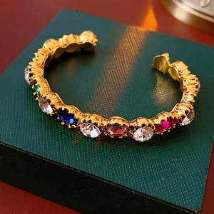 Vintage gold open bangle with multicolored oval crystals on a textured jewelry box
