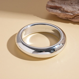 Close-up of a high-polish silver geometric cuff bracelet on a minimalist textured surface