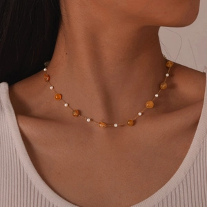 Close-up of gold chain necklace featuring white pearls and amber beads on a model neck