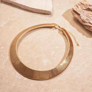 Macro detail of golden geometric metal choker with vertical ribbed texture and clasp