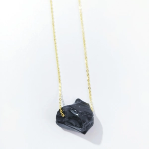 Close-up of a natural raw black stone pendant on a delicate golden chain necklace