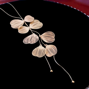 Detail der goldenen Ginkgoblatt-Halskette mit gebürsteter Metallstruktur und feinen Quasten