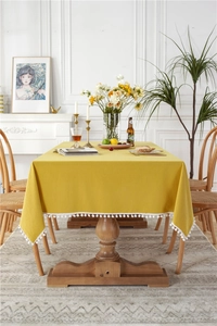 Close-up of yellow cotton tablecloth with white pom-pom fringe on a wooden table