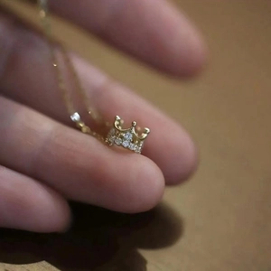 Detailed close-up of a delicate gold crown pendant with sparkling cubic zirconia stones