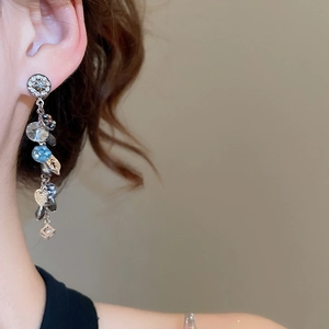 Dettaglio di orecchini pendenti in argento con cristalli blu indossati da una modella