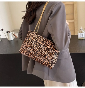 Détail d'un sac à bandoulière léopard avec chaîne dorée porté sur un blazer gris