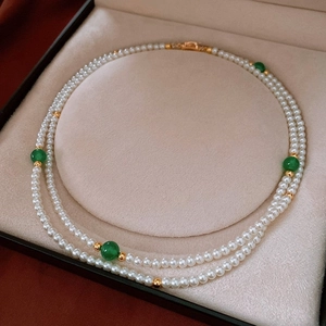 Detail of double-layer white pearl necklace with green beads and gold hardware