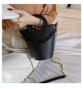 Detail of black bucket bag with circular metal handle and chunky chain on white bedding