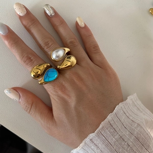 Close-up of gold titanium steel rings featuring turquoise and pearl teardrop stones