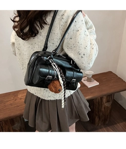 Detail of black glossy PU leather underarm bag with front pockets and cute bear charm