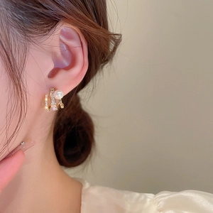 Detail of gold claw-shaped earrings with micro-set rhinestones and a pearl on a model