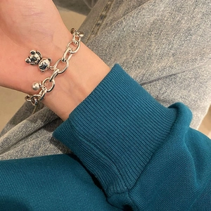 Detail shot of a silver chain bracelet featuring a bear charm worn on a wrist
