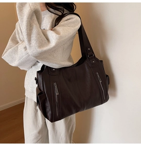 Detail of a large chocolate brown leather tote bag with functional dual zippers on a model