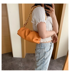 Detail of orange pleated cloud bag featuring a thick gold metal chain shoulder strap