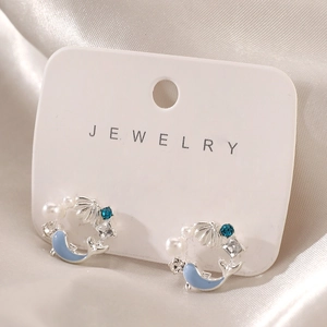 Detailed shot of starfish shell earrings with blue rhinestones and pearls on white satin