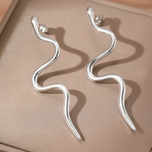 Minimalist silver wavy snake drop earrings with a polished metallic finish on a leather box