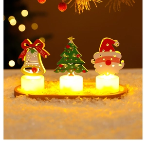 Close-up of LED Christmas candle lights with Santa and tree motifs on snowy wood tray