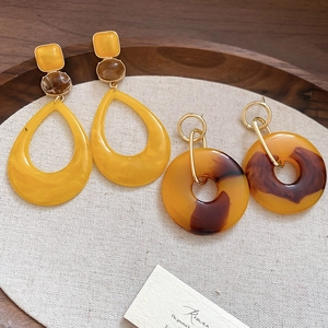 Macro shot of geometric resin drop earrings with amber tortoise textures on a linen tray