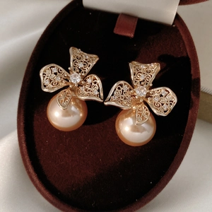 Détail de boucles d'oreilles fleurs dorées avec zircons et perle dorée suspendue