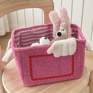 Pink plush monster storage basket with cute wings and striped lining on wooden stool