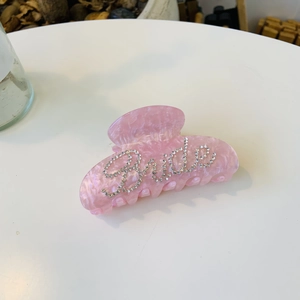 Dettaglio molletta per capelli in acrilico rosa marmorizzato con scritta Bride in strass