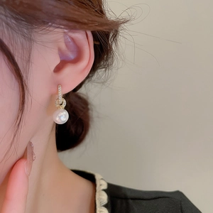 Gros plan sur des boucles d'oreilles dorées avec cristaux de zircon et perle blanche pendante