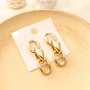 Exaggerated gold chain earrings on a beige ceramic tray for a trendy night club jewelry style