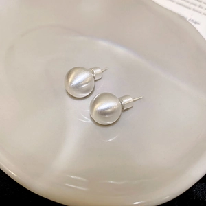 Macro shot of silver brushed ball stud earrings on a ceramic plate with matte texture