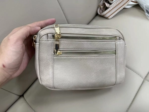 Detail view of smooth beige PU leather crossbody bag featuring gold double zip pockets