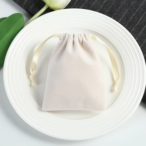 Close-up of a velvet drawstring jewelry pouch in cream white on a white porcelain dish