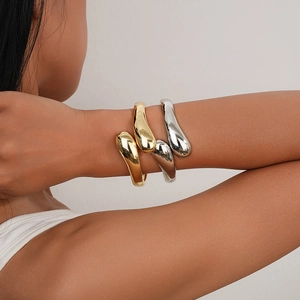 Close-up of minimalist gold and silver teardrop cuff bracelets worn on a model arm