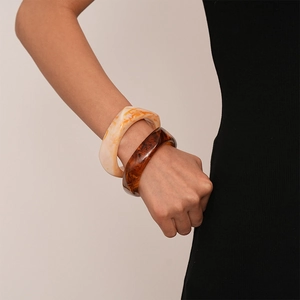 Detail of amber and cream marble acrylic resin bangles on a model wearing black