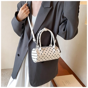 Close-up of white cylindrical PU leather crossbody bag with bold black polka dot pattern