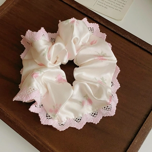 Détail d'un chouchou à fleurs avec dentelle rose posé sur un plateau en bois vintage