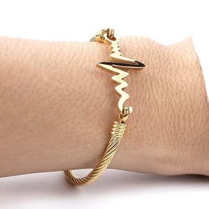 Detail of twisted cable gold heartbeat bracelet worn on wrist for an elegant fit