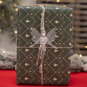 Close-up of a clear acrylic fairy ornament hanging on a green gift box with soft festive lights