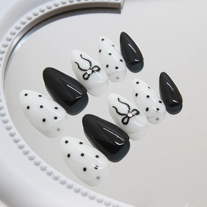 Almond-shaped white polka dot and black bow press-on nails with rhinestones on a tray