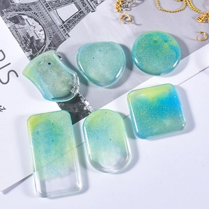 Macro shot of glittery teal resin pendants in heart, oval, and square shapes