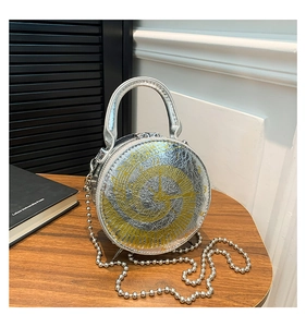 Detail of silver round bag with gold clock face pattern and metal chain on wood table