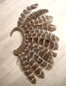 Close-up of bohemian peacock feather ear cuff with golden metal base on wood