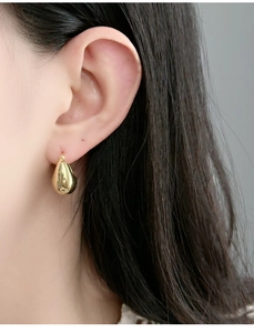 Detailed close-up of a gold teardrop earring with high-polish finish on a model