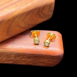 Macro view of gold minimalist stud earrings with round zircons on warm wood