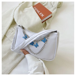 Close-up of a white shoulder bag featuring a blue butterfly pendant and silver chain strap