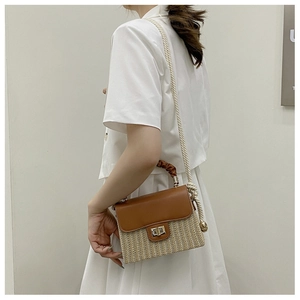 Detail of a straw box bag with brown leather flap and metallic twist lock closure
