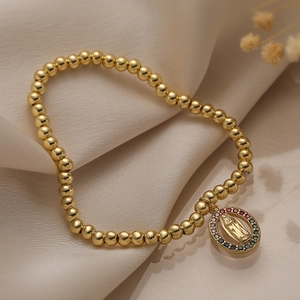 Goldenes Perlenarmband mit buntem Zirkonia-Maria-Anhänger auf beigem Seidenstoff