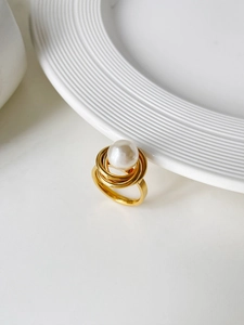Gros plan d'une bague spirale dorée ornée d'une grande perle blanche sur céramique