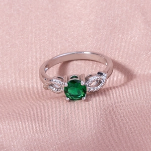 Macro detail of silver ring with green gemstone on soft pink satin fabric background