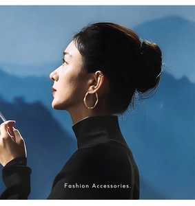 Close-up of golden spiral hoop earrings on model with blue mountain backdrop